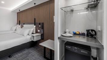A modern hotel room with a large bed, a small desk, a built-in coffee maker, and a microwave.