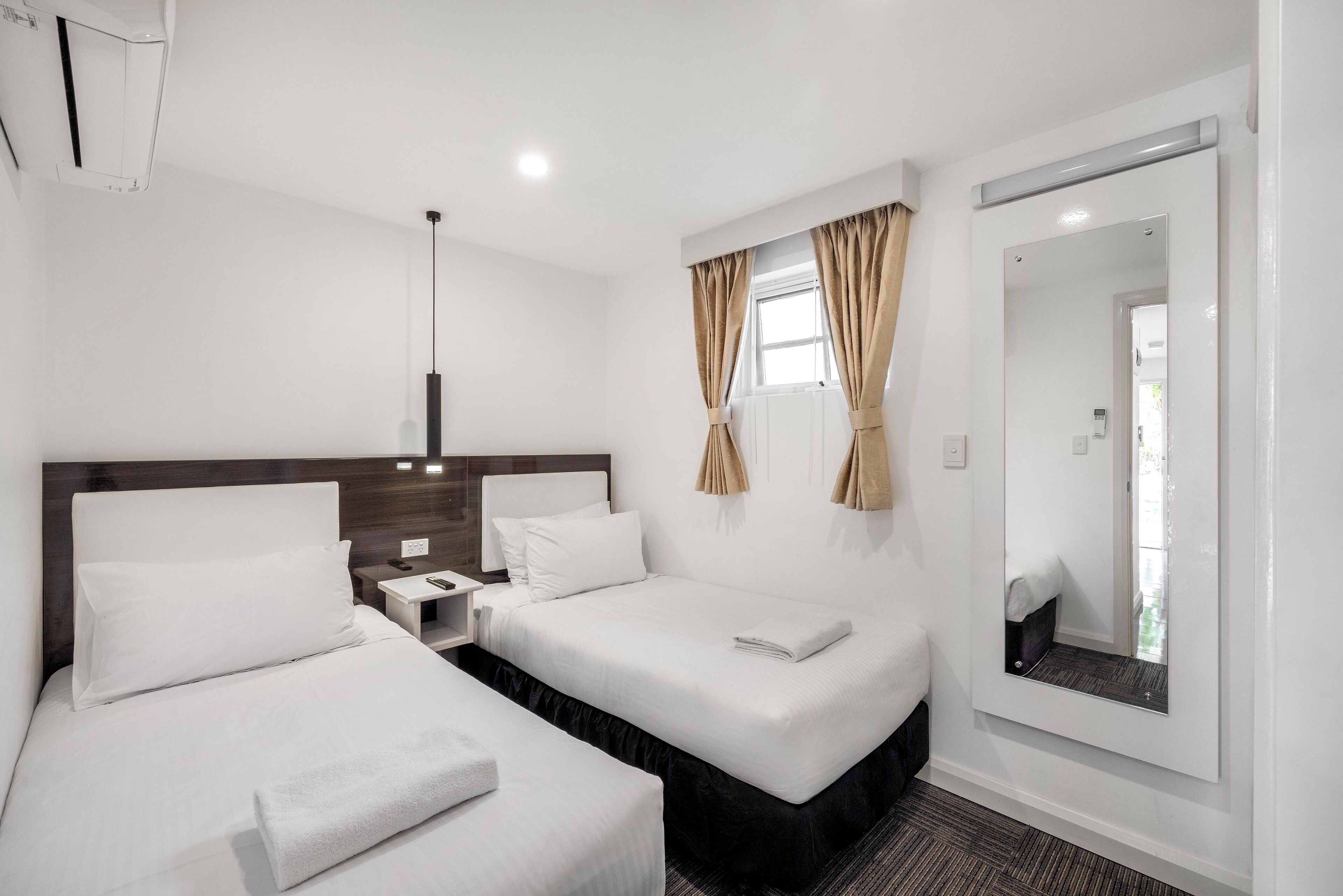 A hotel room with two beds, a nightstand, a mirror, and a window with curtains.