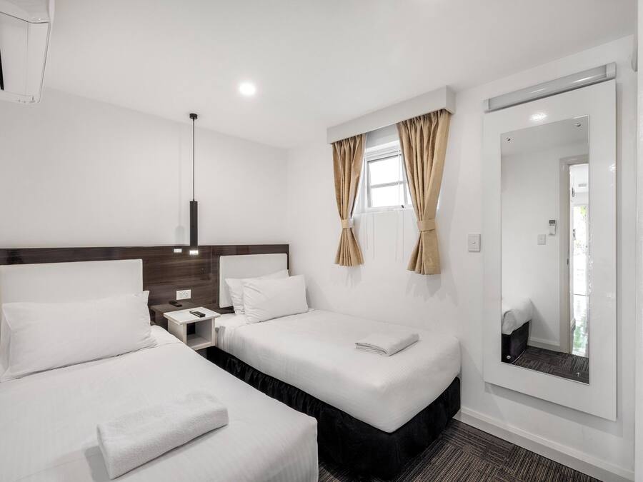 A hotel room with two beds, a nightstand, a mirror, and a window with curtains.