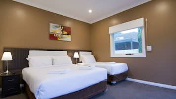 A hotel room with two beds, a nightstand, a lamp, a painting on the wall, and a window with blinds.