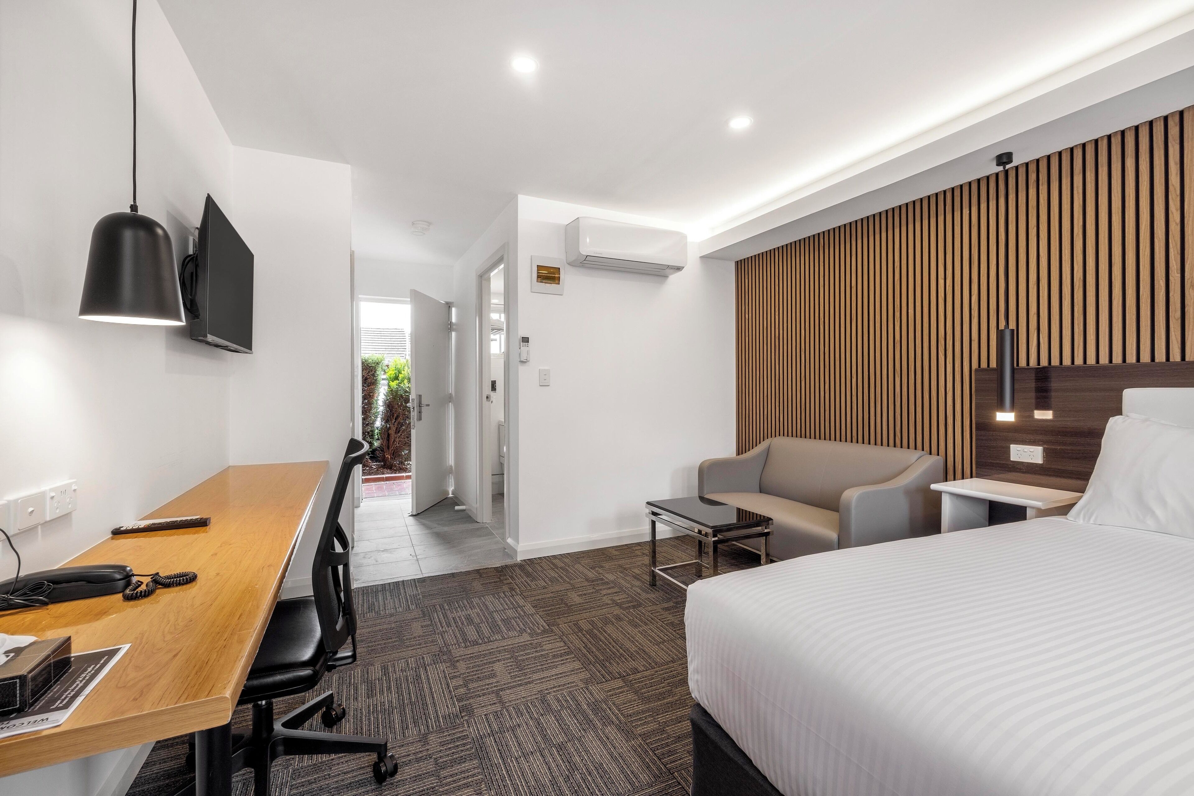 A modern hotel room with a wooden desk, a bed, a sofa, and a TV.