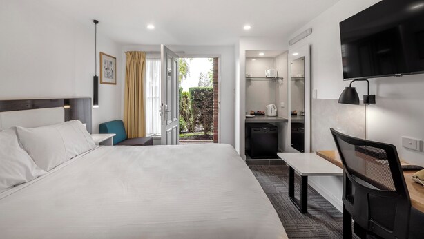 Habitación de hotel con una cama grande, un escritorio, una silla, un televisor, una kitchenette y vistas al exterior.