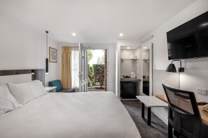 Habitación de hotel con una cama grande, un escritorio, una silla, un televisor, una kitchenette y vistas al exterior.