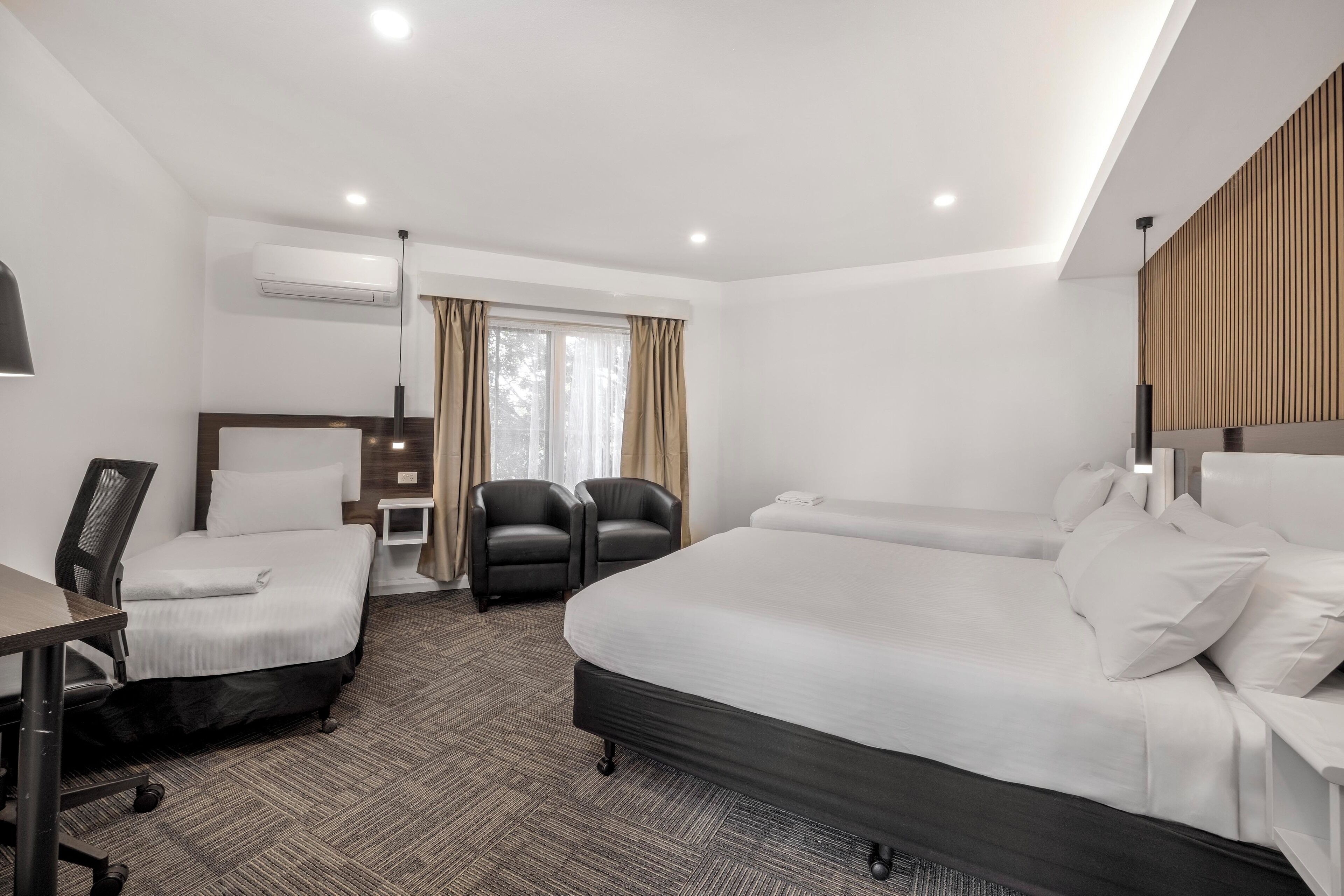 A hotel room with a large bed, two smaller beds, a desk, and a chair.