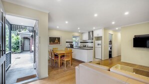 Una cocina moderna con armarios blancos, un comedor con mesa y sillas de madera, y un televisor integrado.