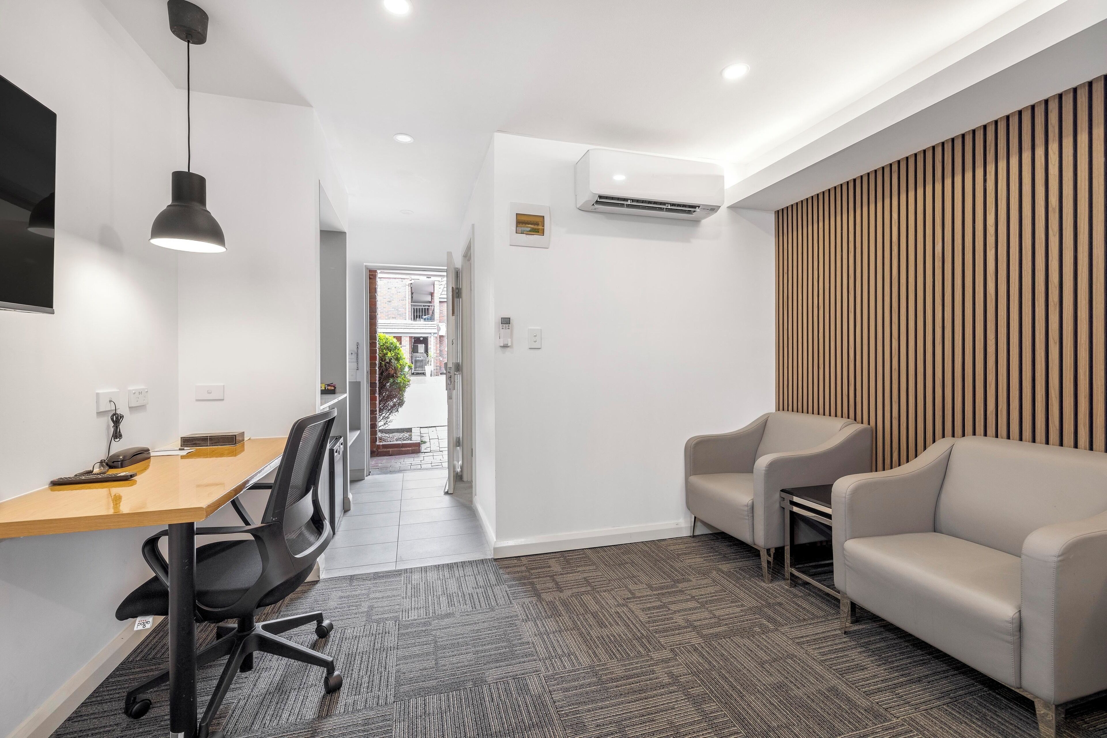 A modern office space with a wooden desk, black office chair, and a beige sofa.