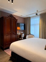 Une chambre d’hôtel avec un grand lit, une armoire en bois, un bureau avec une lampe et un téléviseur.