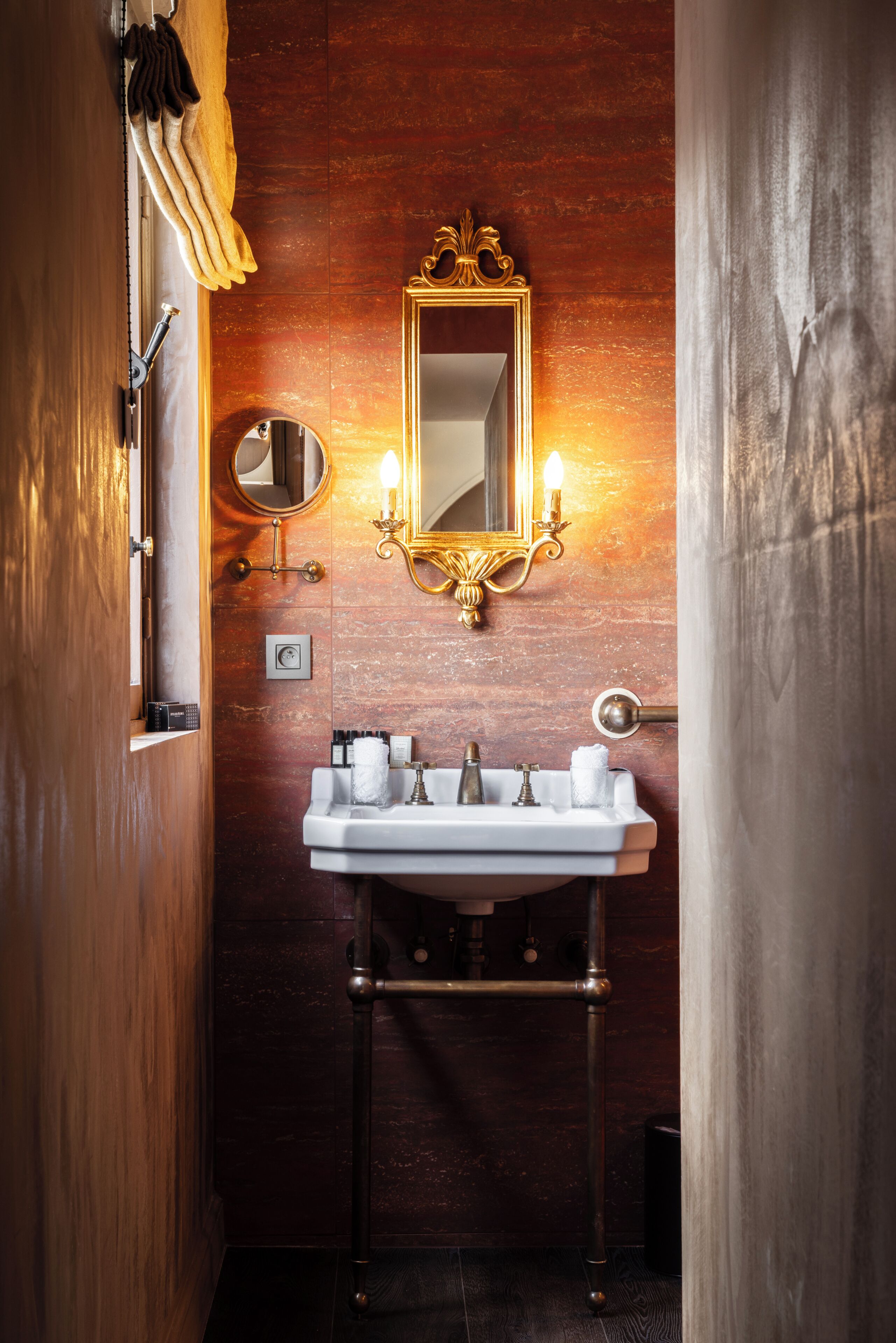 Een badkamer met een houten wand, een witte wastafel met een gouden kraan, een spiegel met een gouden lijst en een handdoekhouder.