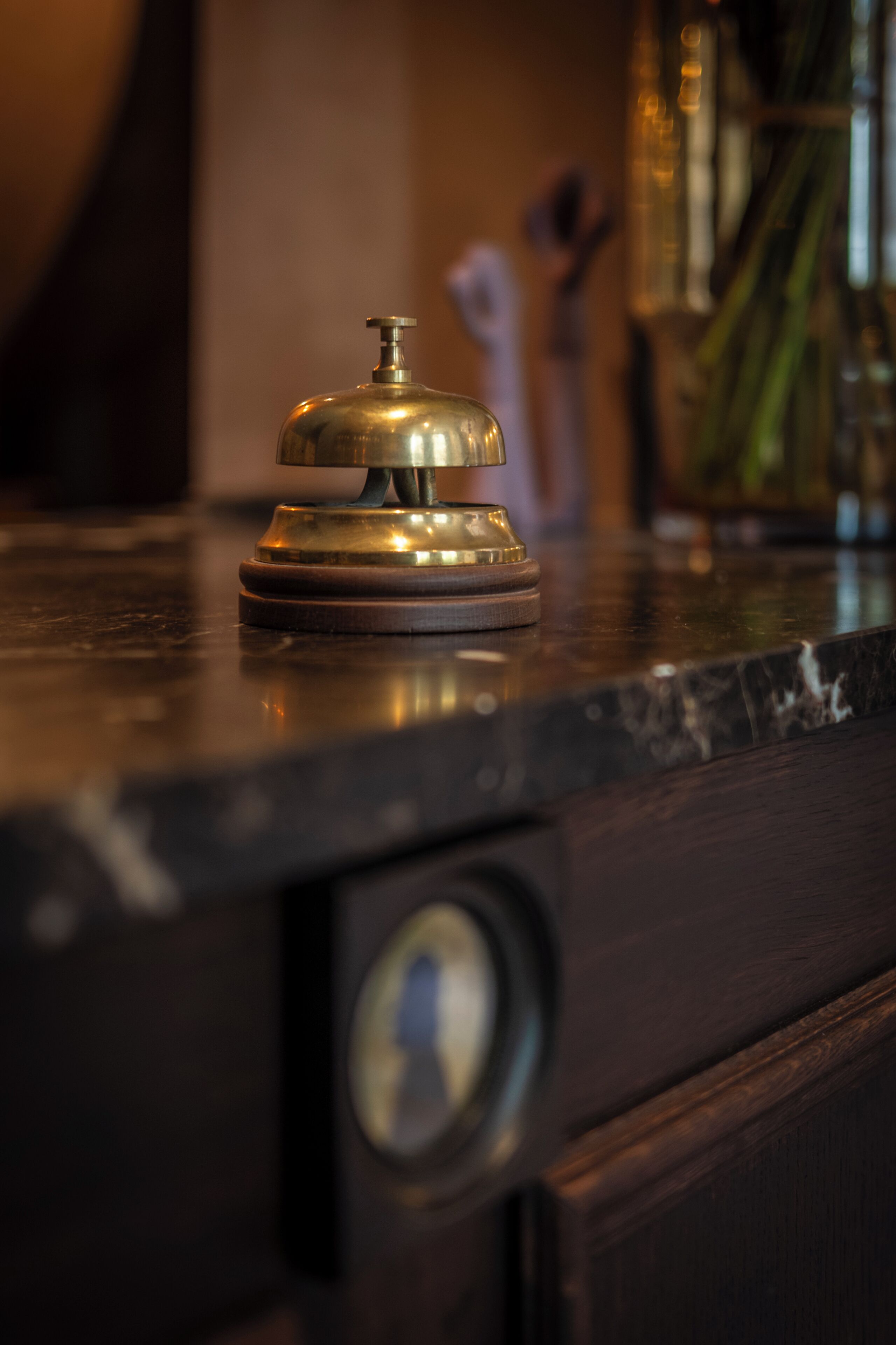 A brass bell on a dark wooden counter, a keyhole, and a blurred background with a plant.
