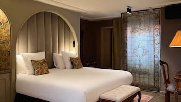 A large bed with a headboard, a bedside table, a chair, and a window with a view.