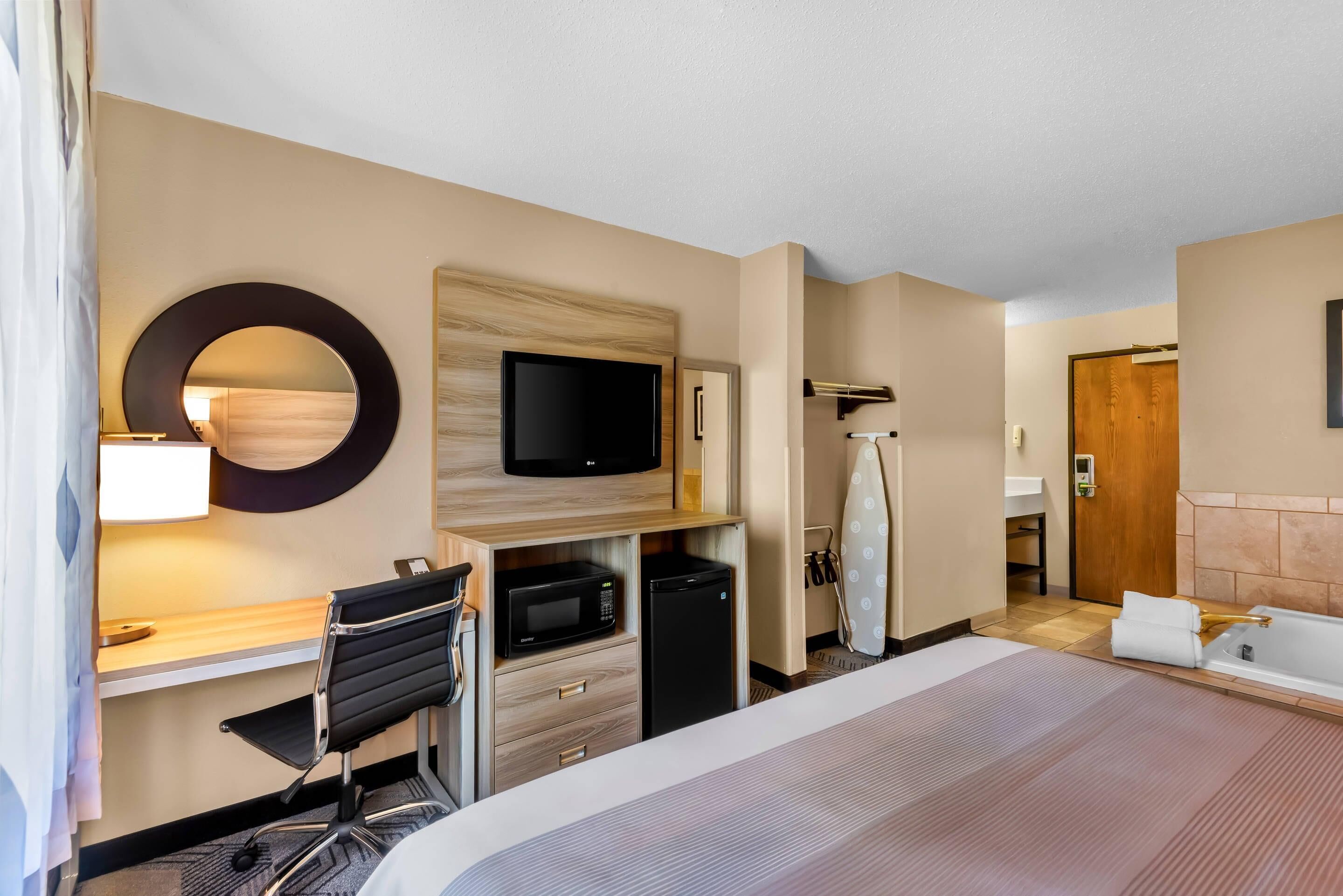 Habitación de hotel con cama, escritorio con silla, televisor, microondas y refrigerador pequeño.