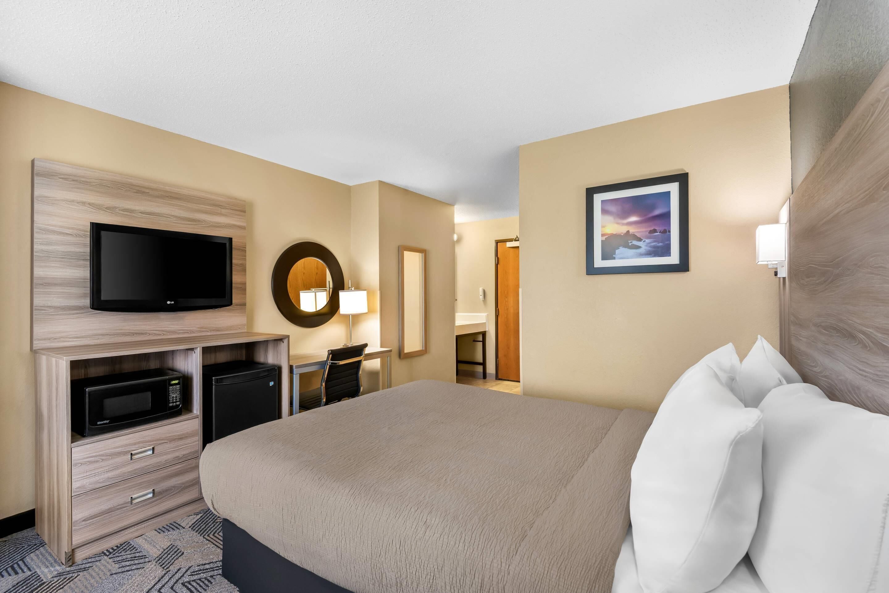 A hotel room with a bed, a TV, a microwave, a desk, and a bathroom visible in the background.