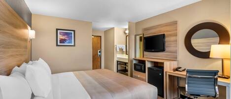 Una habitación de hotel con cama, escritorio, televisor y espejo.