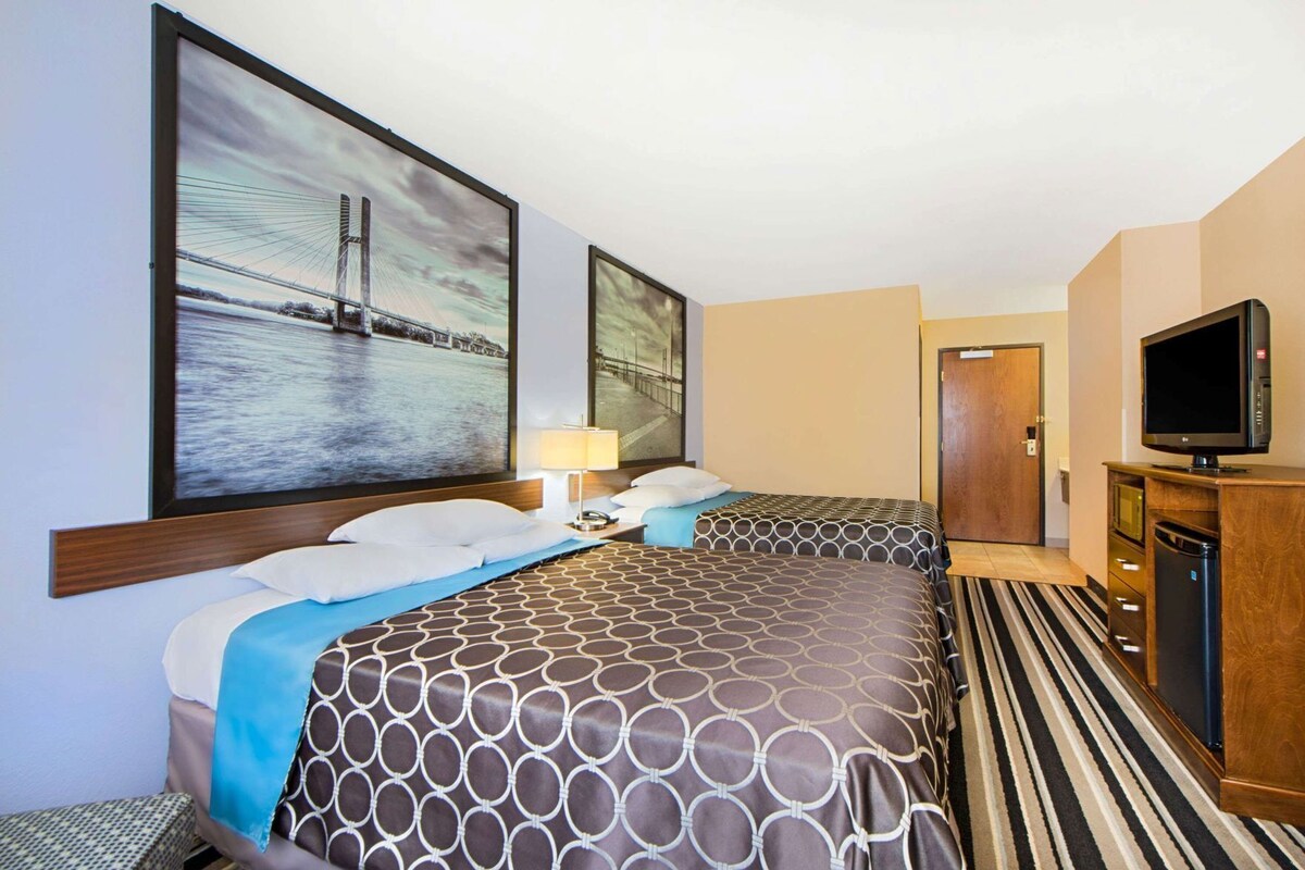 Een hotelkamer met twee bedden, een televisie, een bureau met een computer en kunstwerken aan de muren.