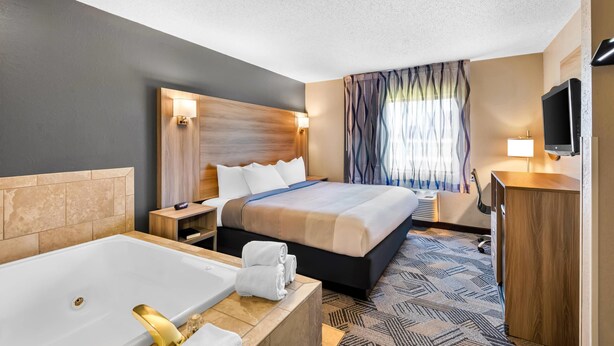 Une chambre d’hôtel avec deux lits, une grande baignoire, une télévision et une fenêtre avec des rideaux.