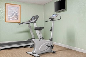 A room with two stationary bikes, a treadmill, a framed picture on the wall, and a TV mounted above.