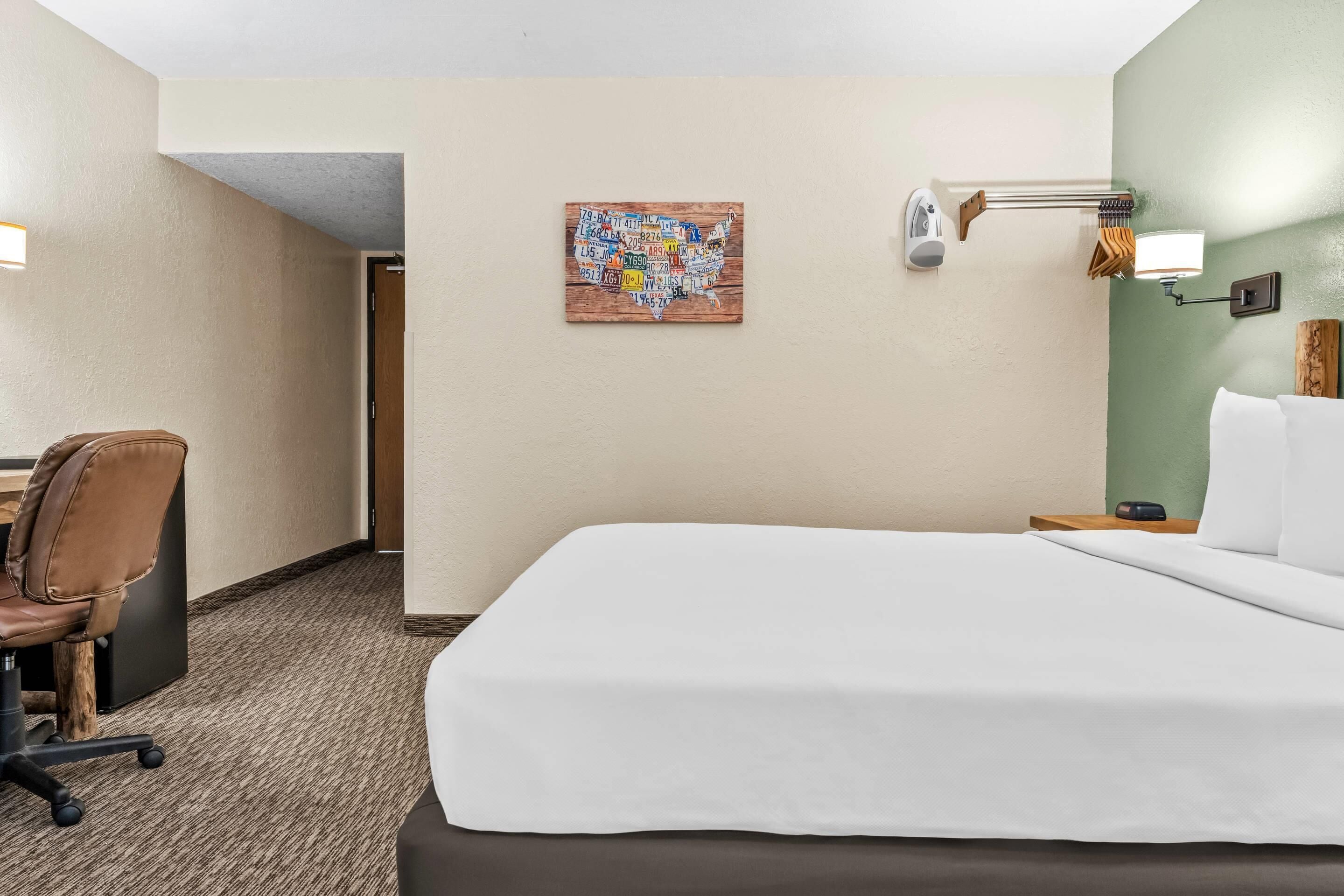 A hotel room with a large bed, a desk with a chair, a wall-mounted lamp, and a map artwork on the wall.