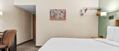 A hotel room with a large bed, a desk with a chair, a wall-mounted lamp, and a map artwork on the wall.