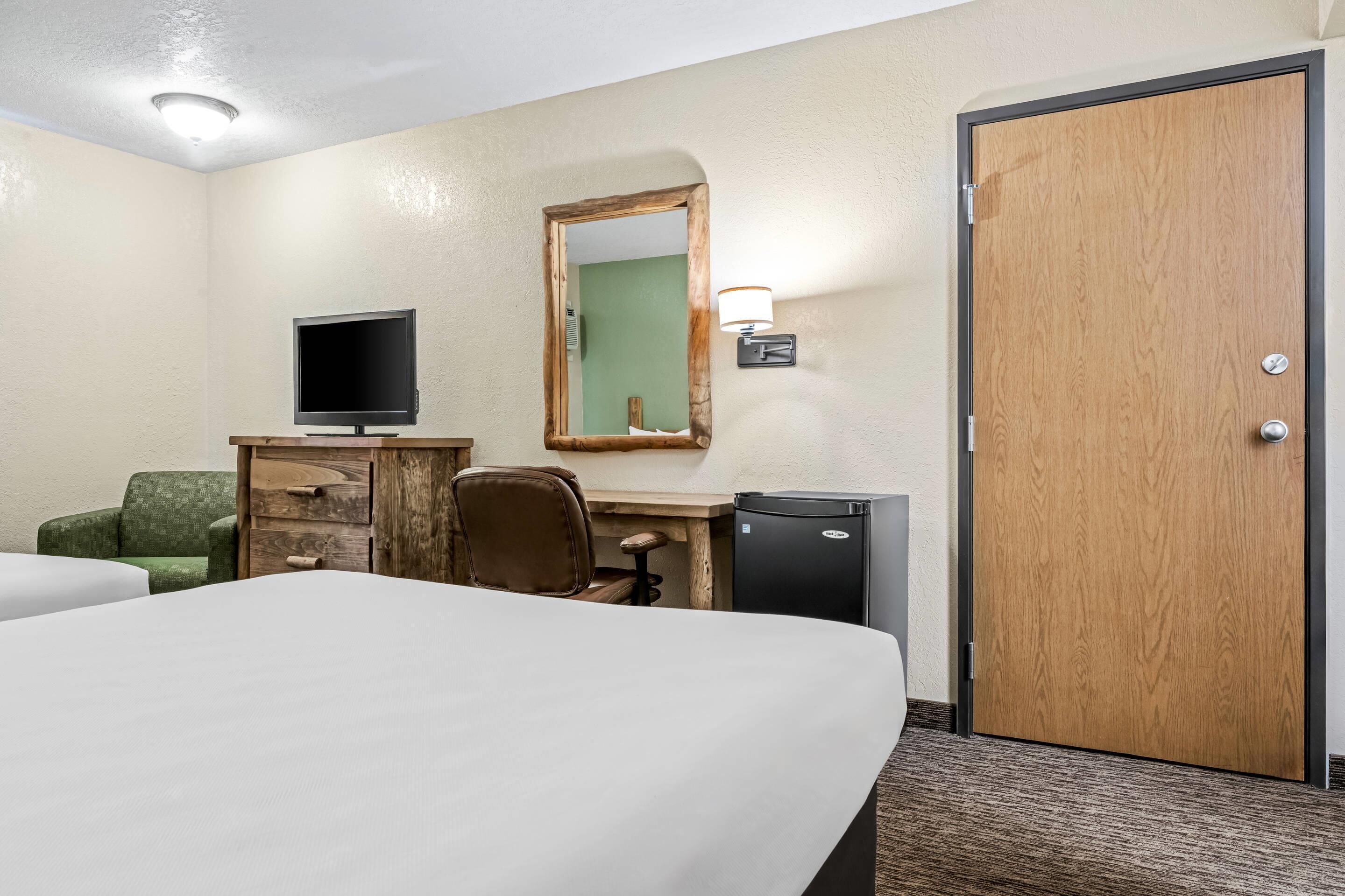 A hotel room with a bed, a desk with a television, a chair, a dresser, a mirror, and a door.