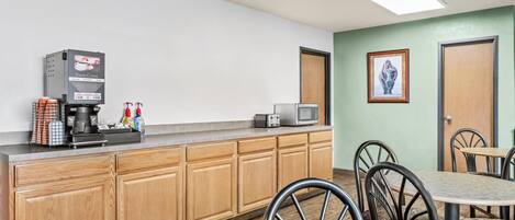 A kitchenette with a coffee machine, microwave, and toaster. There are wooden cabinets and a dining area with chairs and a table.