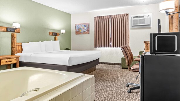 Quarto de hotel com uma cama grande, uma banheira, uma escrivaninha com um computador, uma cadeira e uma janela com cortinas.
