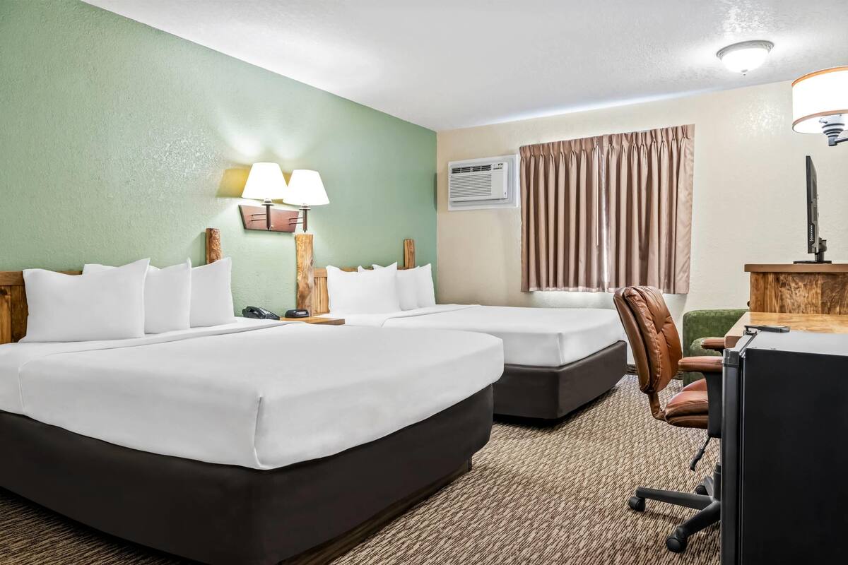 A hotel room with two beds, a desk, a chair, a lamp, and an air conditioning unit.