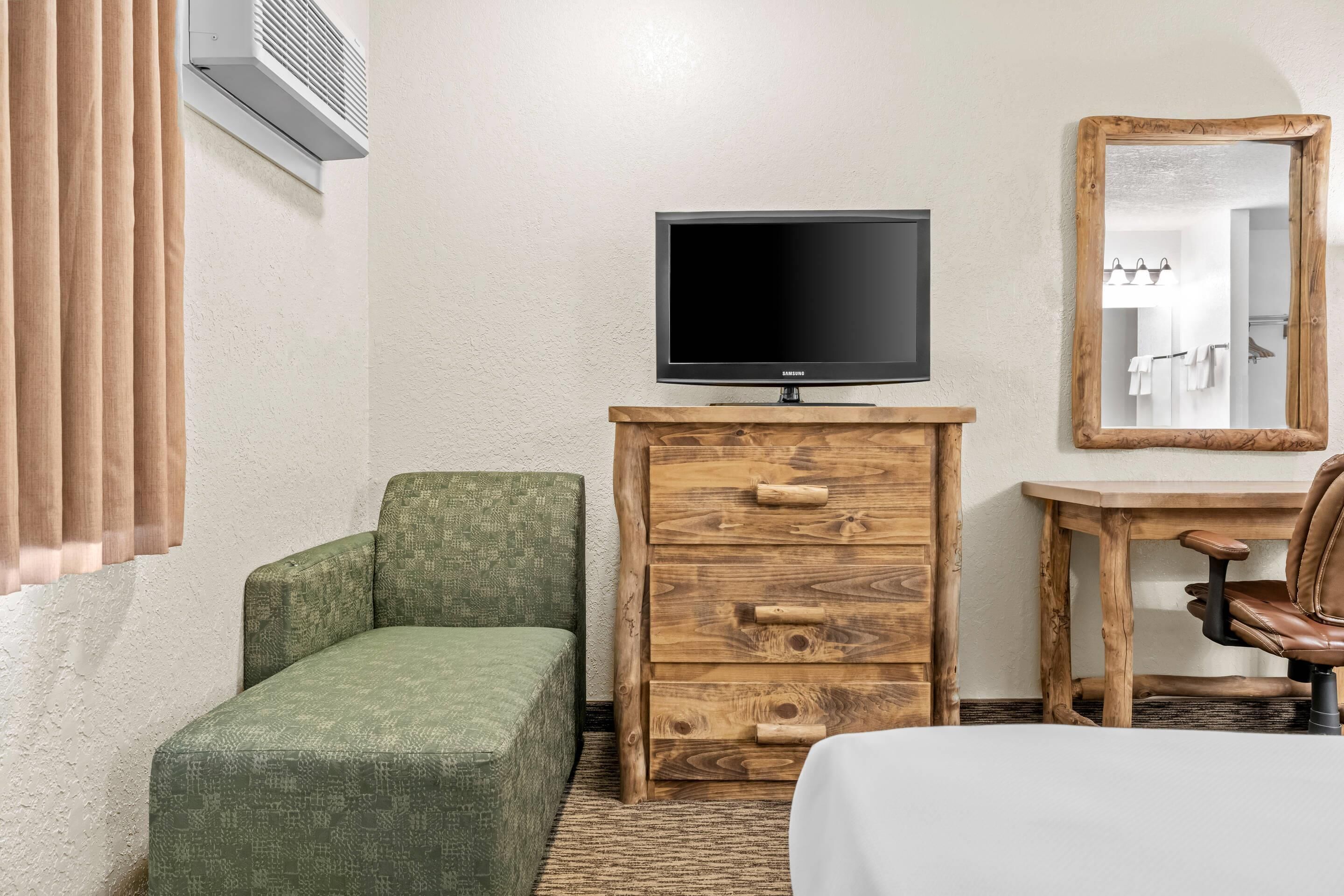 A room with a green sofa, a wooden dresser with a television on top, a wooden chair, and a mirror on the wall.