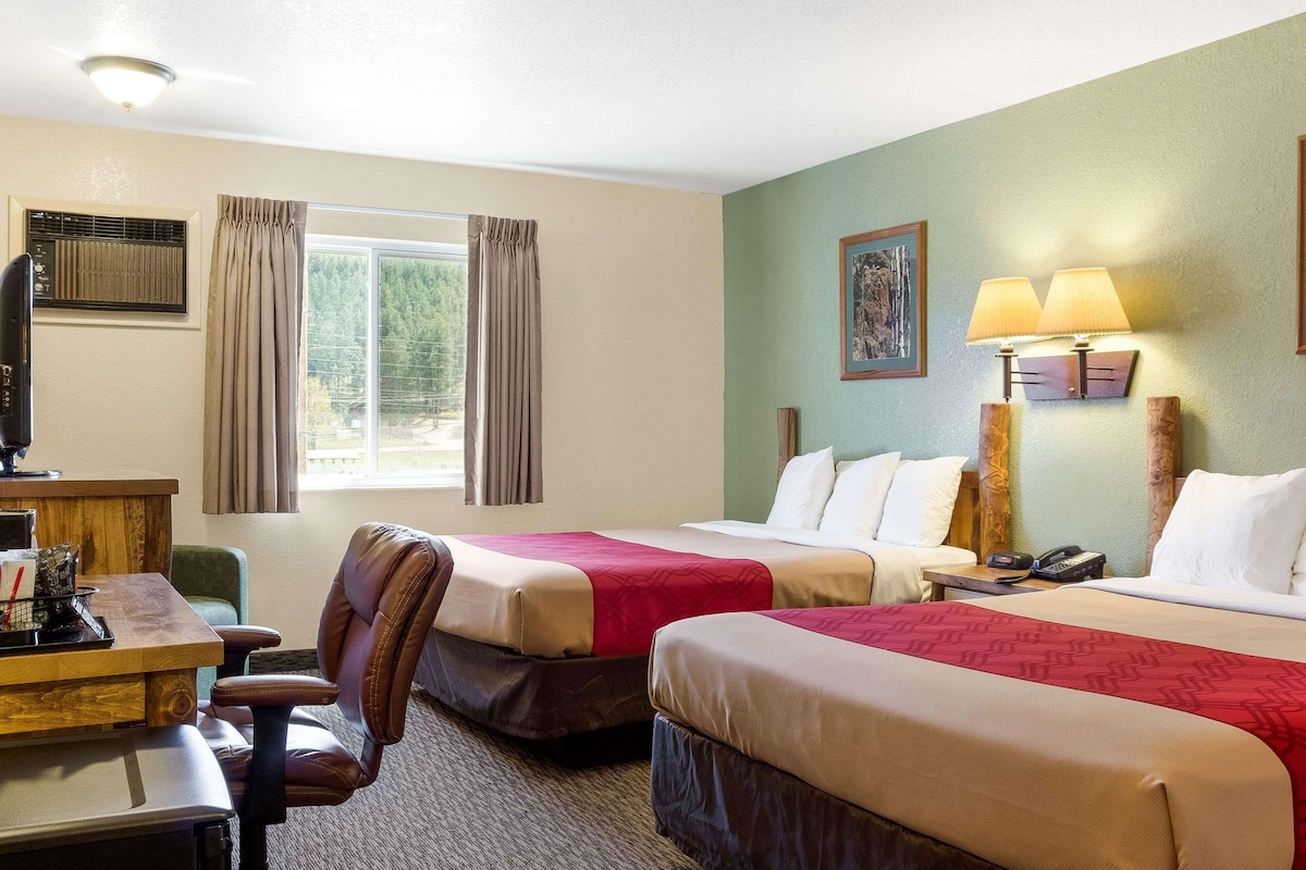 A hotel room with two beds, a desk, a chair, a lamp, and a painting on the wall.