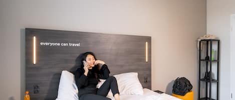 A modern hotel room with a large bed, a nightstand with a bottle, and a bookshelf.
