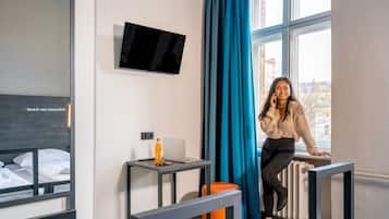 A modern hotel room with a bed, a desk with a laptop, a TV, and a large window with curtains.