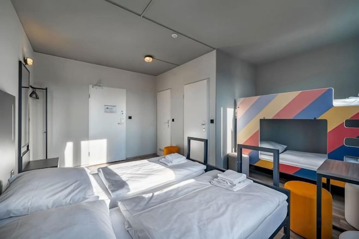 A hotel room with two beds, a desk, and a colorful wall design.
