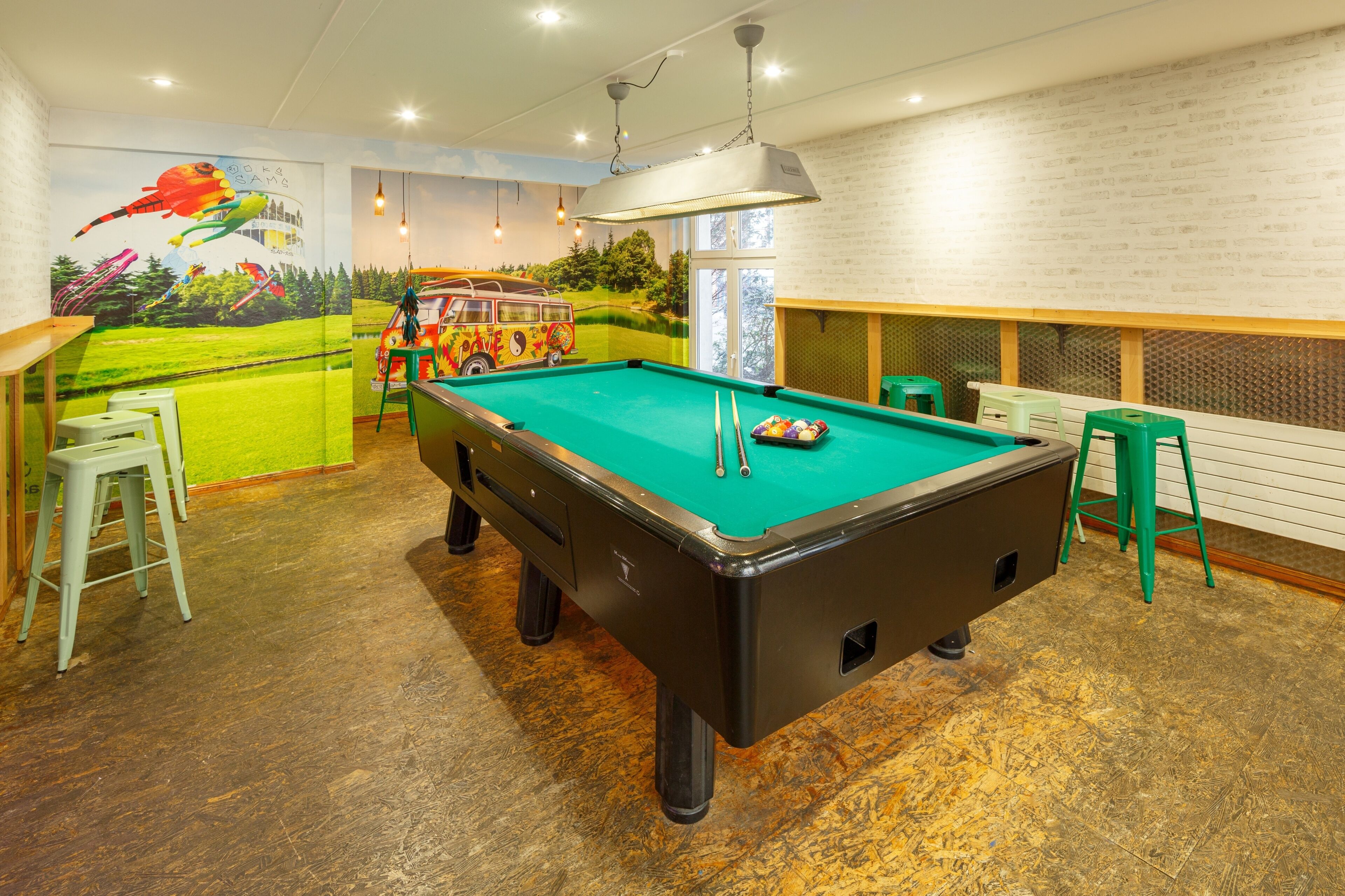 A pool table with stools, a mural, and a brick wall.