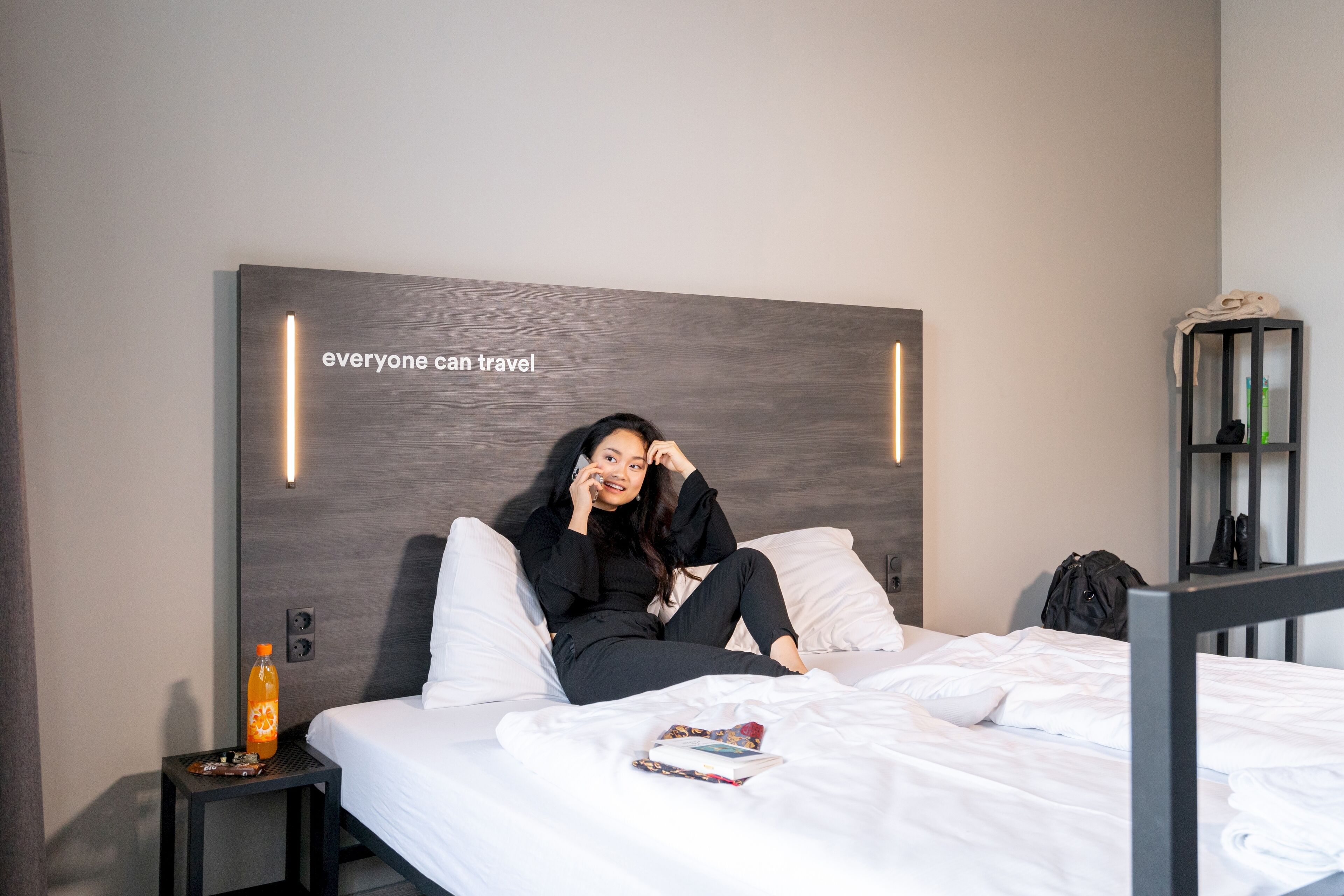 Una habitación de hotel moderna con una cama grande, una mesita de noche con una botella y una pared con una cita motivacional.
