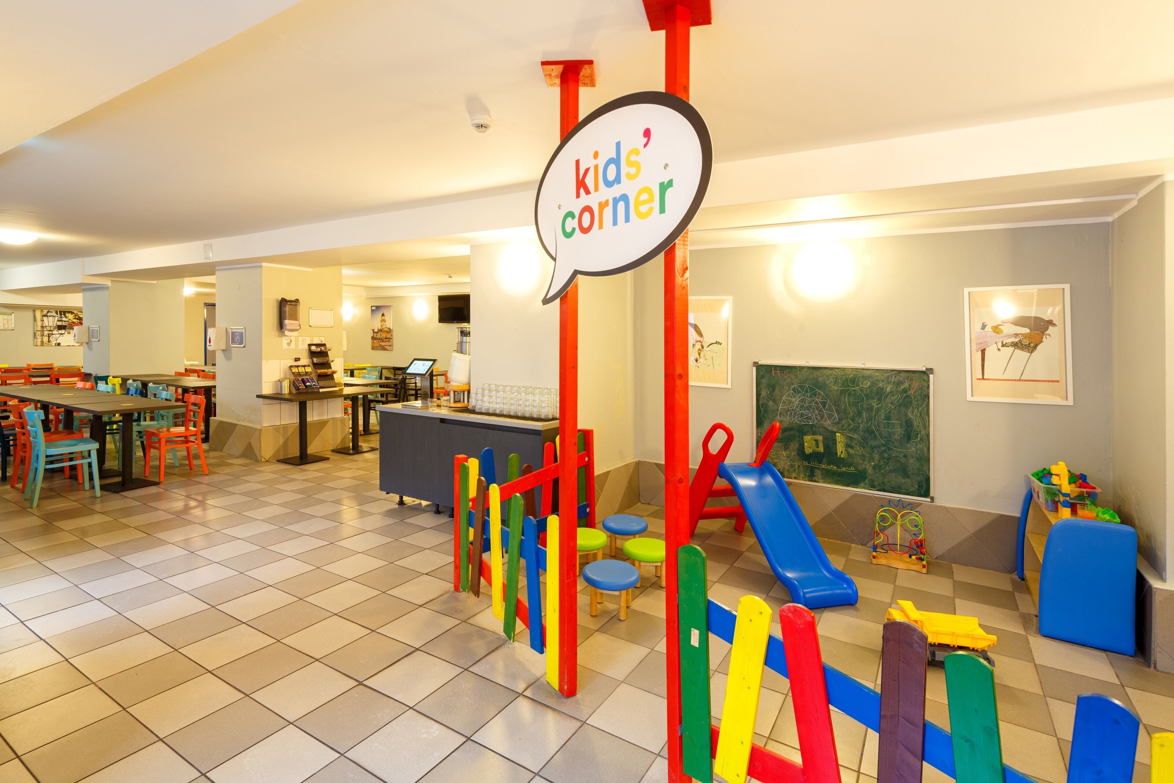Un área de juegos infantiles con estructuras de juego coloridas y una zona de comedor con mesas y sillas.