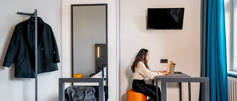 Habitación de hotel con cama, escritorio, silla, televisión y espejo.