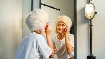 Eine Person trägt vor einem Spiegel mit Wandleuchte Make-up auf.