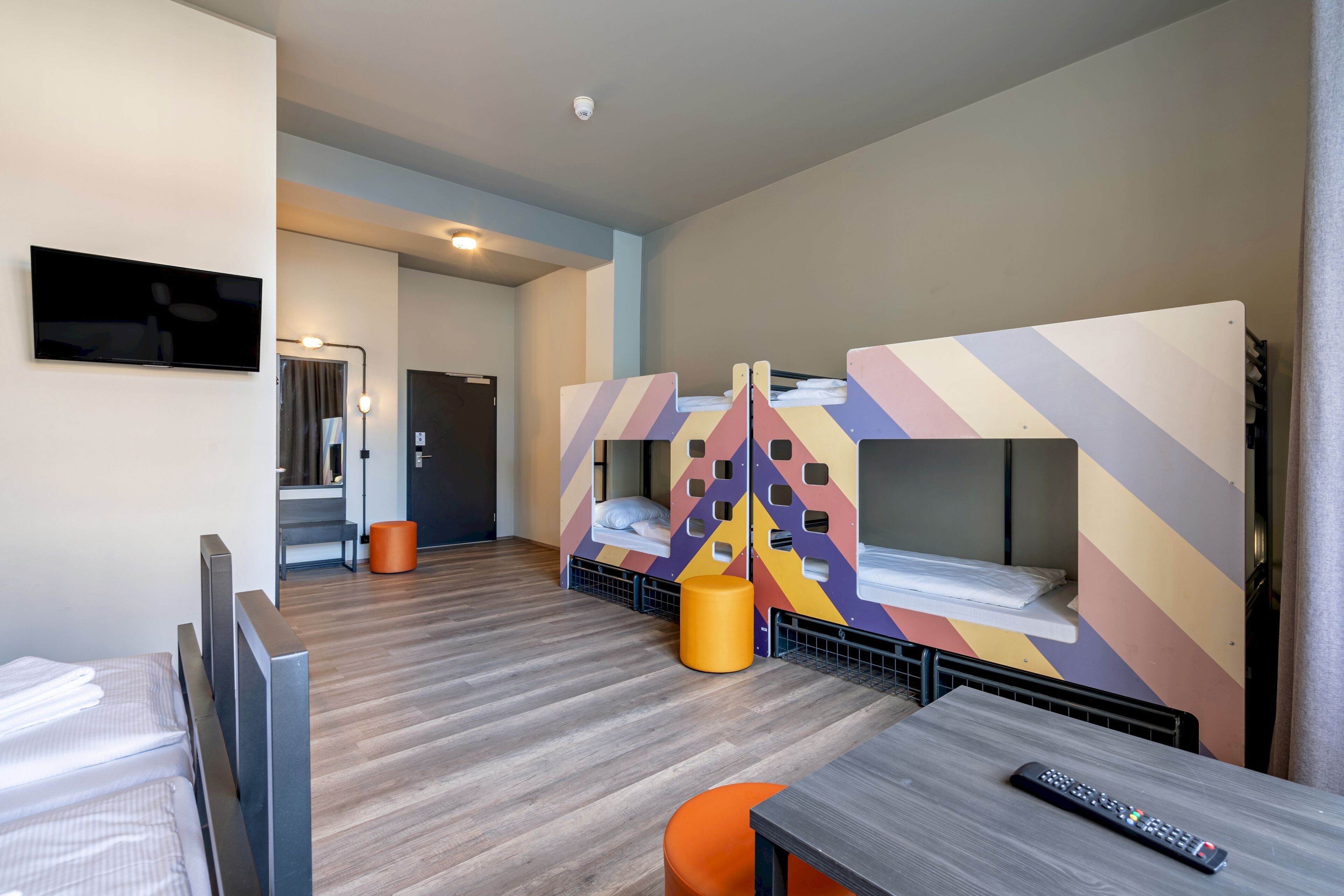 A modern hotel room with bunk beds, a flat-screen TV, a wooden floor, and a small table with a remote control.