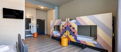 A modern hotel room with bunk beds, a flat-screen TV, a wooden floor, and a small table with a remote control.