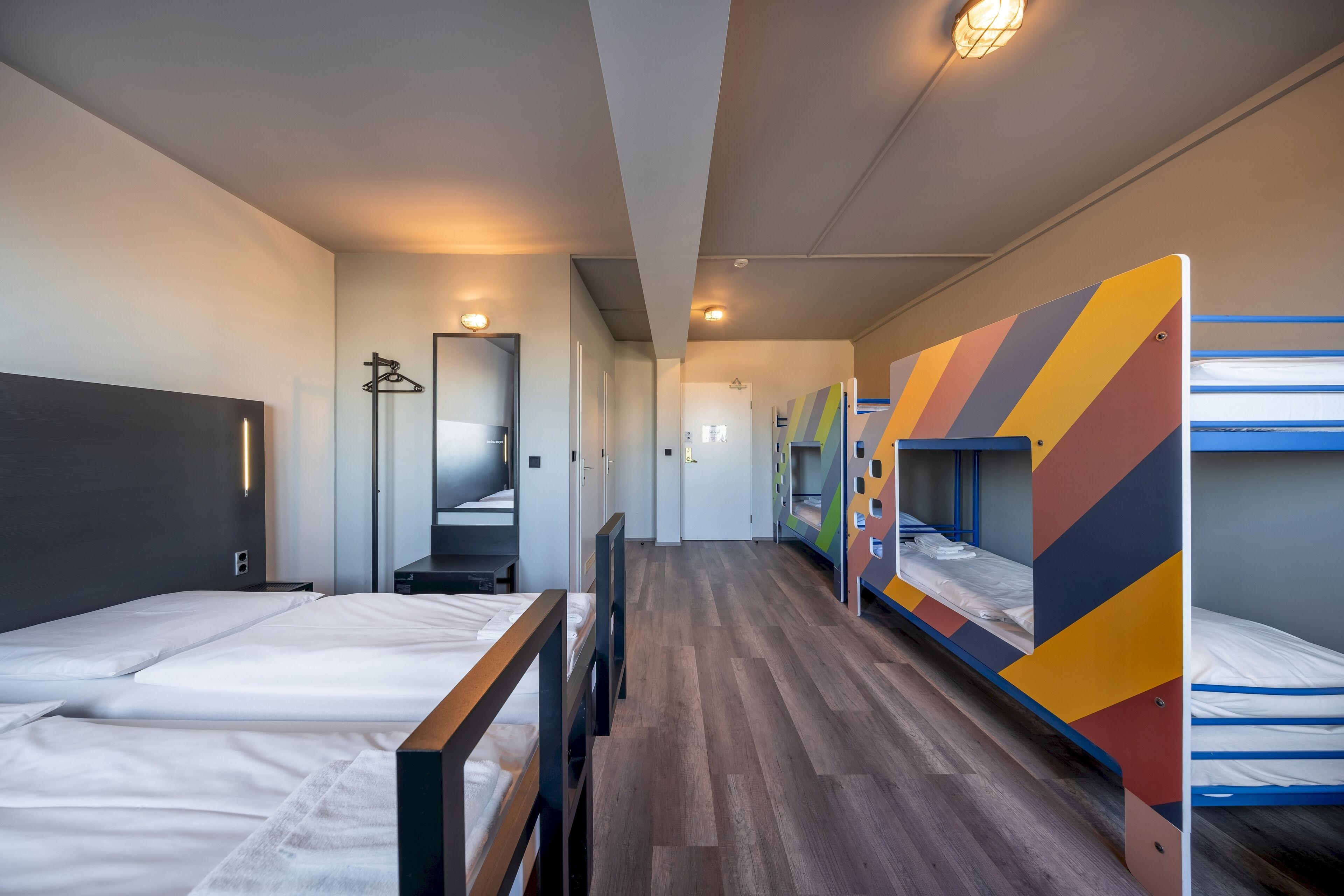 A hotel room with bunk beds, a wooden headboard, a mirror, and a hallway leading to other rooms.