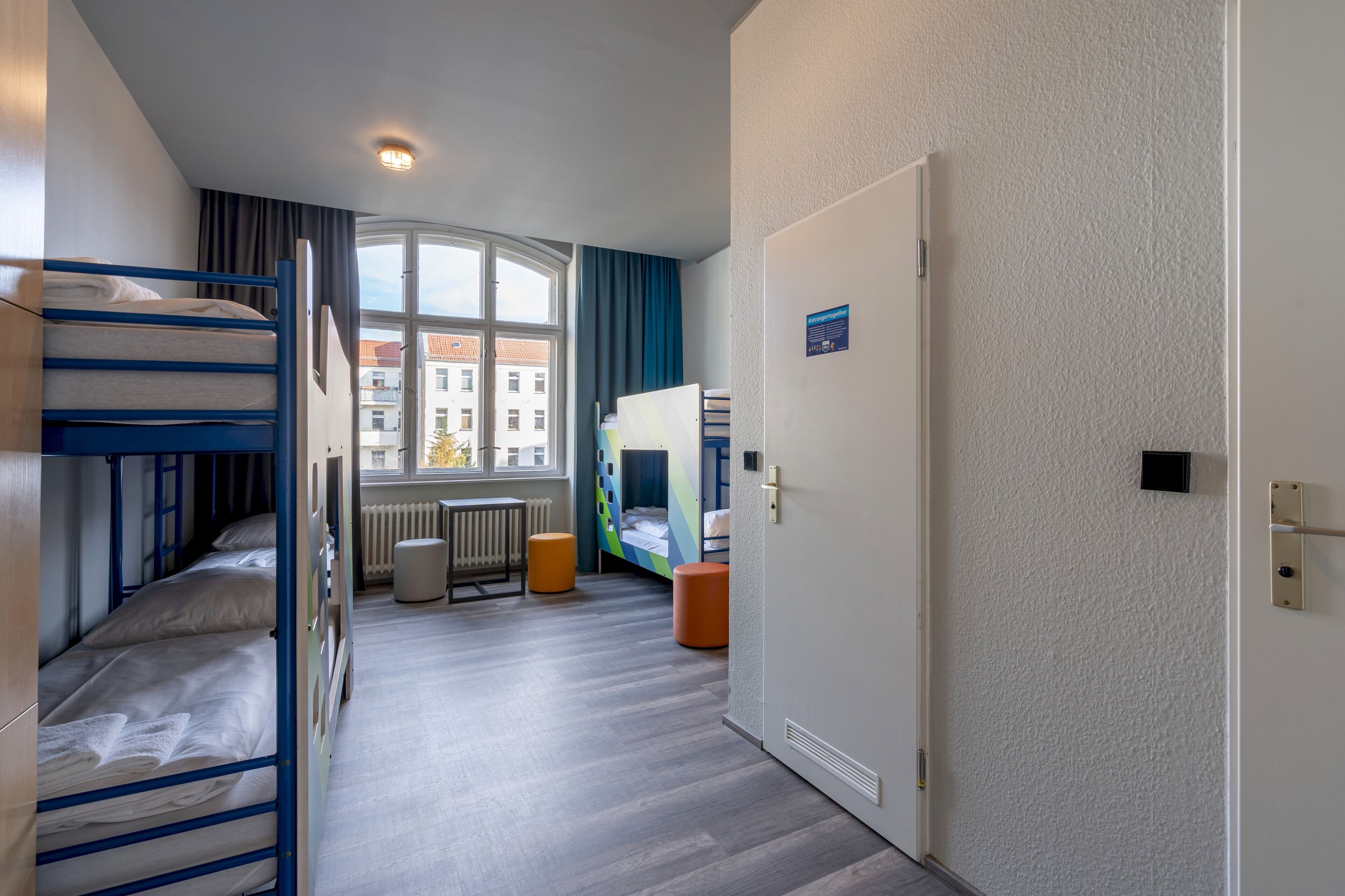 Un dormitorio con camas literas, una ventana con cortinas, un radiador y una puerta con un cartel.