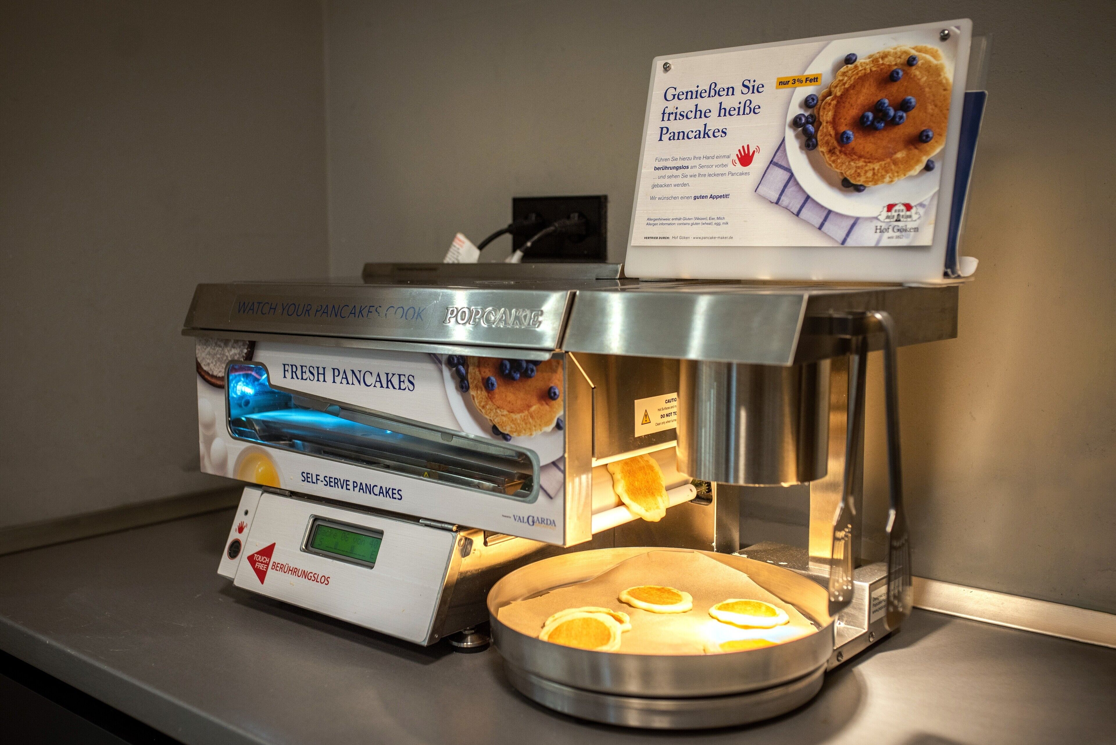 A self-serve pancake machine with fresh pancakes and a sign advertising them.