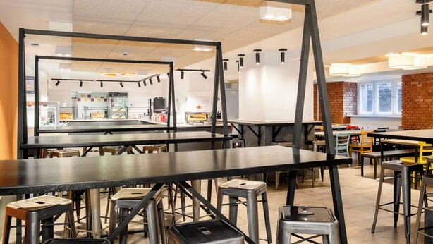 A modern restaurant interior with high tables, stools, and a brick accent wall. - a&o Berlin Friedrichshain (Berlin)