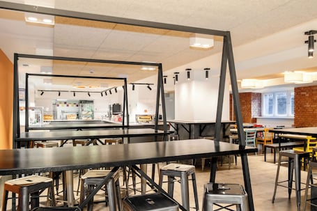 A modern restaurant interior with high tables, stools, and a brick accent wall.