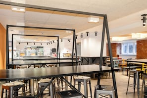 A modern restaurant interior with high tables, stools, and a brick accent wall.
