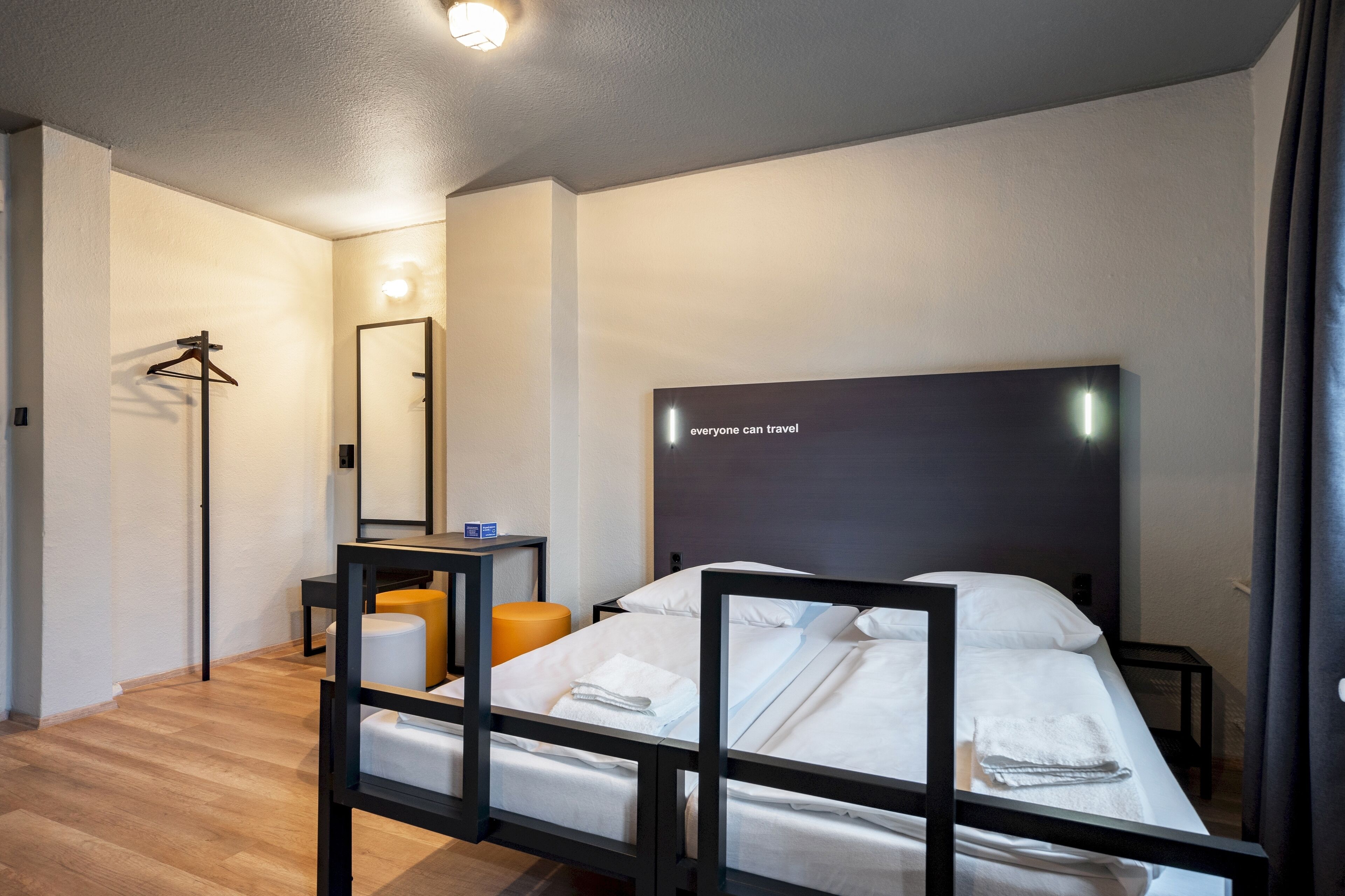 A modern hotel room with a large bed, a desk, a chair, and a mirror.