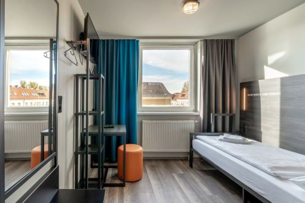 Ett modernt hotellrum med en säng, ett skrivbord, en stol och ett fönster med gardiner.