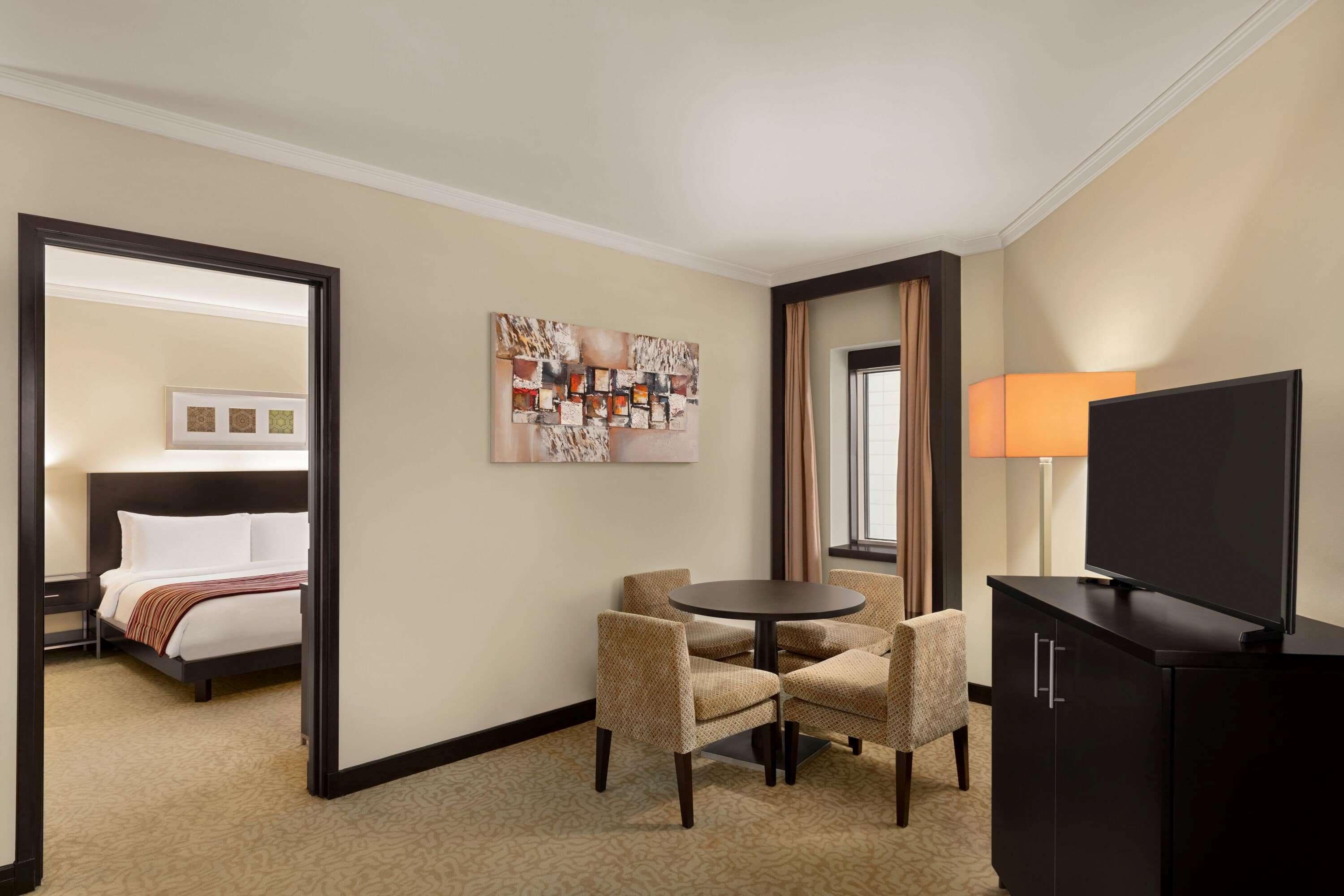 Une chambre d’hôtel avec un lit, un bureau, une chaise, une table, un téléviseur et un tableau au mur.