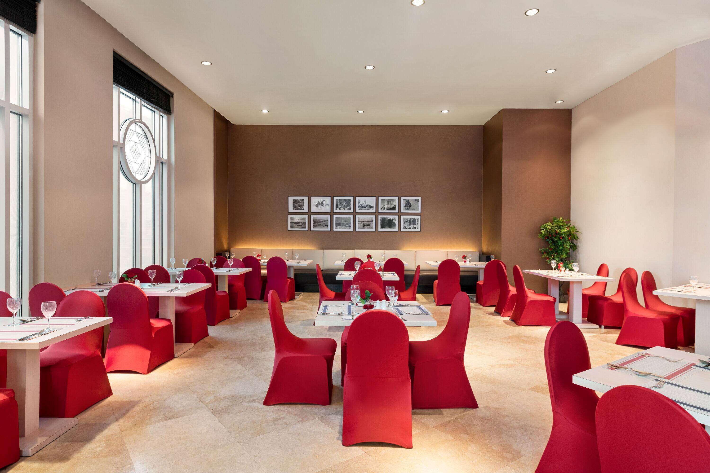 A spacious conference room with multiple tables and chairs, large windows, and a wall with framed pictures.