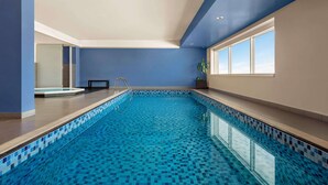 A swimming pool with blue mosaic tiles, a sunlit room with blue walls, and a window providing natural light.