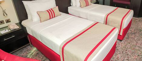 Une chambre d’hôtel avec deux lits, une table de chevet avec un téléphone et une chaise rouge.